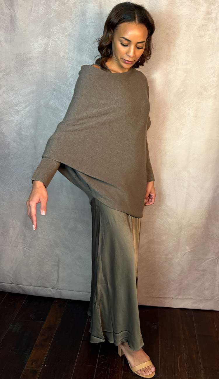 A woman wearing an asymmetrical sweater and a matching silky dress against a neutral background