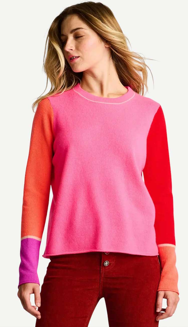 Woman wearing a pink and red color block sweater with red pants on a white background