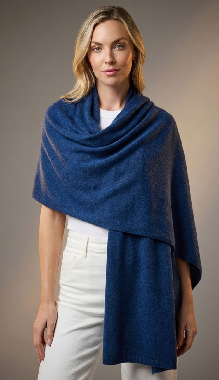 Woman wearing a denim breezy travel wrap shawl over a white outfit against a neutral background