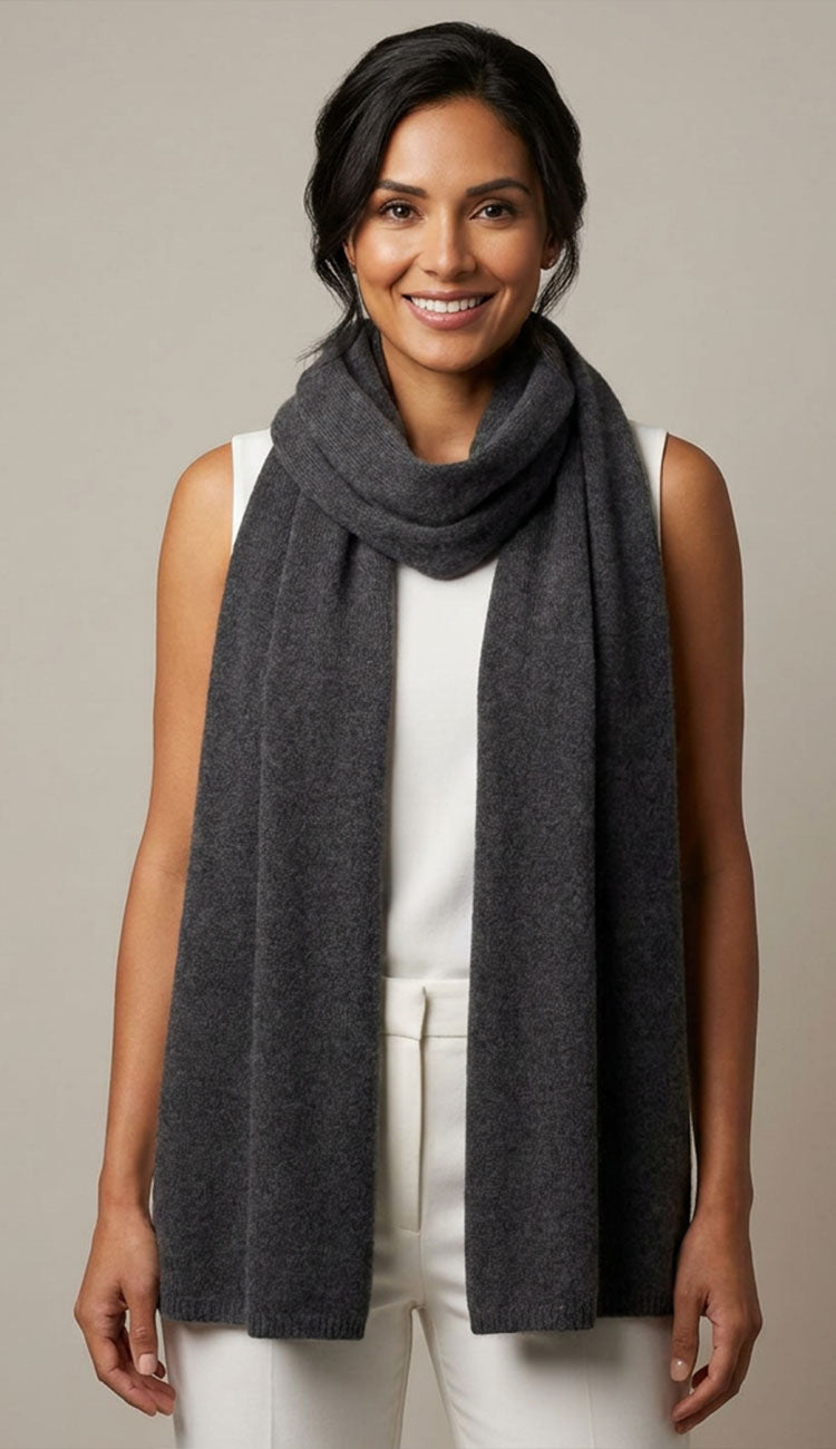 Woman wearing a graphite gray breezy travel wrap scarf over a white top and pants on a beige background