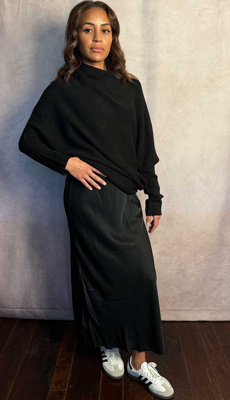 A women wearing a Little black silky dress paired with a black sweater on a beige background