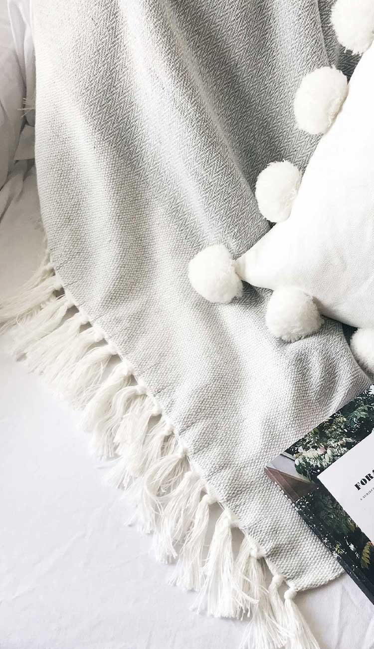 A light grey cotton and bamboo throw blanket draped elegantly with a decorative pillow beside it.