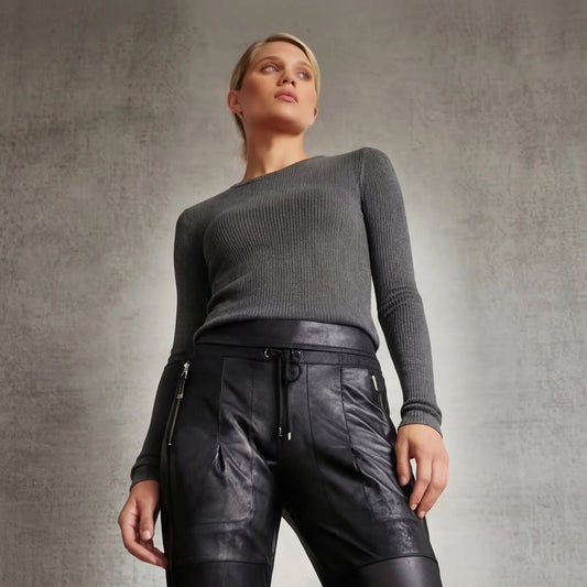 A woman standing in a gray Goldie long sleeve t and vegan leather candy pants in black with a beige background. 