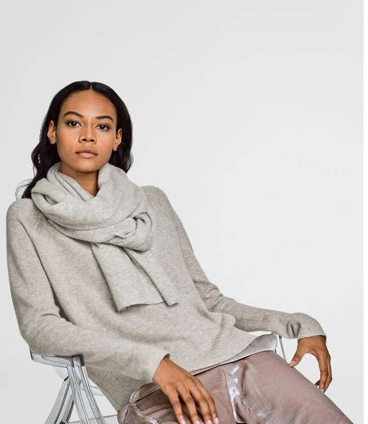 Woman wearing a white and warren cashmere sweater and travel wrap in grey cashmere