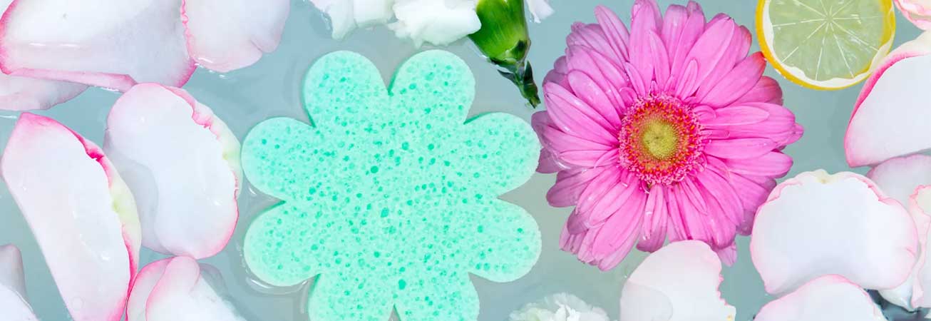 spongelle body sponge floating in water with flowers, petals and lemon slice