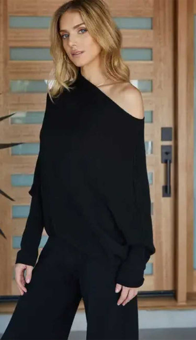 Woman wearing a black off-shoulder top and black pants in front of a wooden door.
