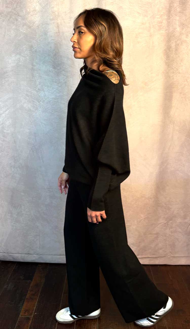 Person wearing a black top and pant outfit with a textured background