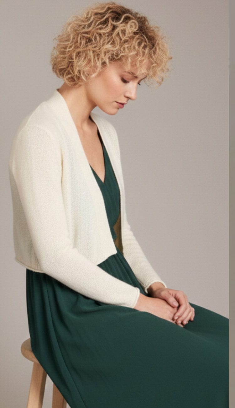 Woman seated wearing the Alashan Cashmere cropped 100% cashmere shrunken cardigan in ivory with long sleeves and an open-front design