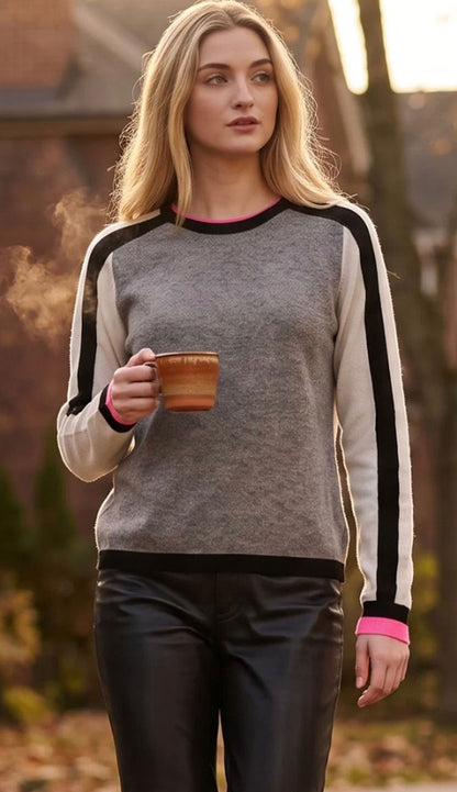 woman wearing the color code crew sweater in grey tones with a black stripe and hot pink cuff trim. woman is holding a cup and wearing leather pants
