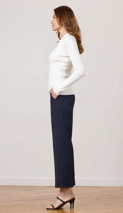 The side view of a woman wearing Grace Needle Line Navy Stripe pants with a white fitted top on a white background.