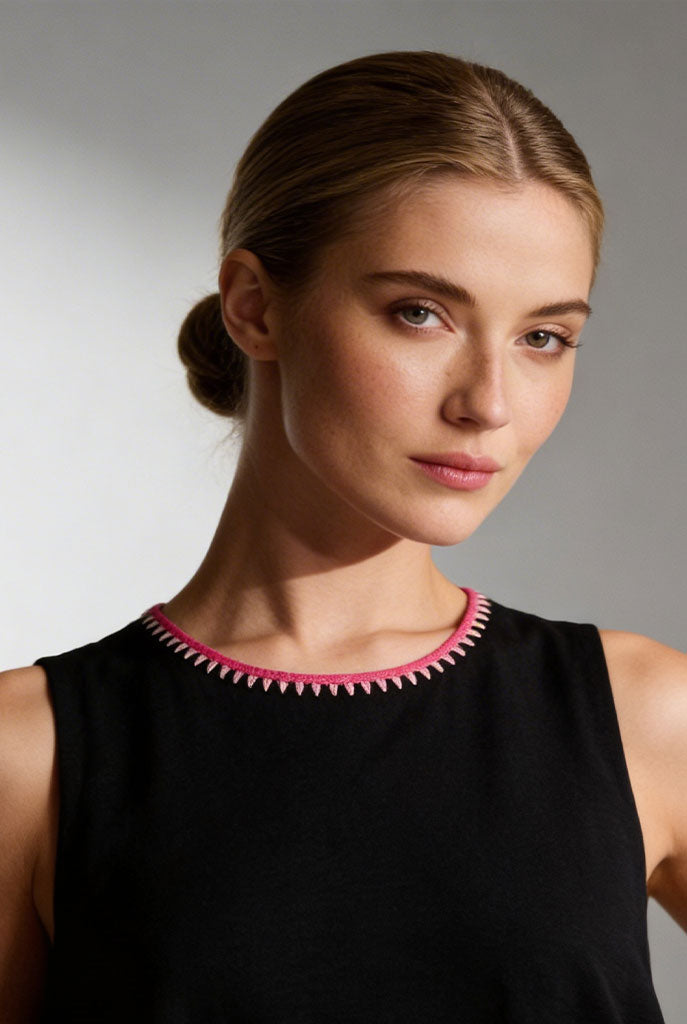 Woman wearing a black sleeveless dress with a pink detailed neckline against a gray background