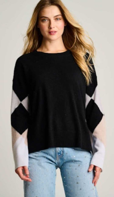 Woman wearing a black sweater with an argyle sleeve pattern with light blue jeans on a plain background