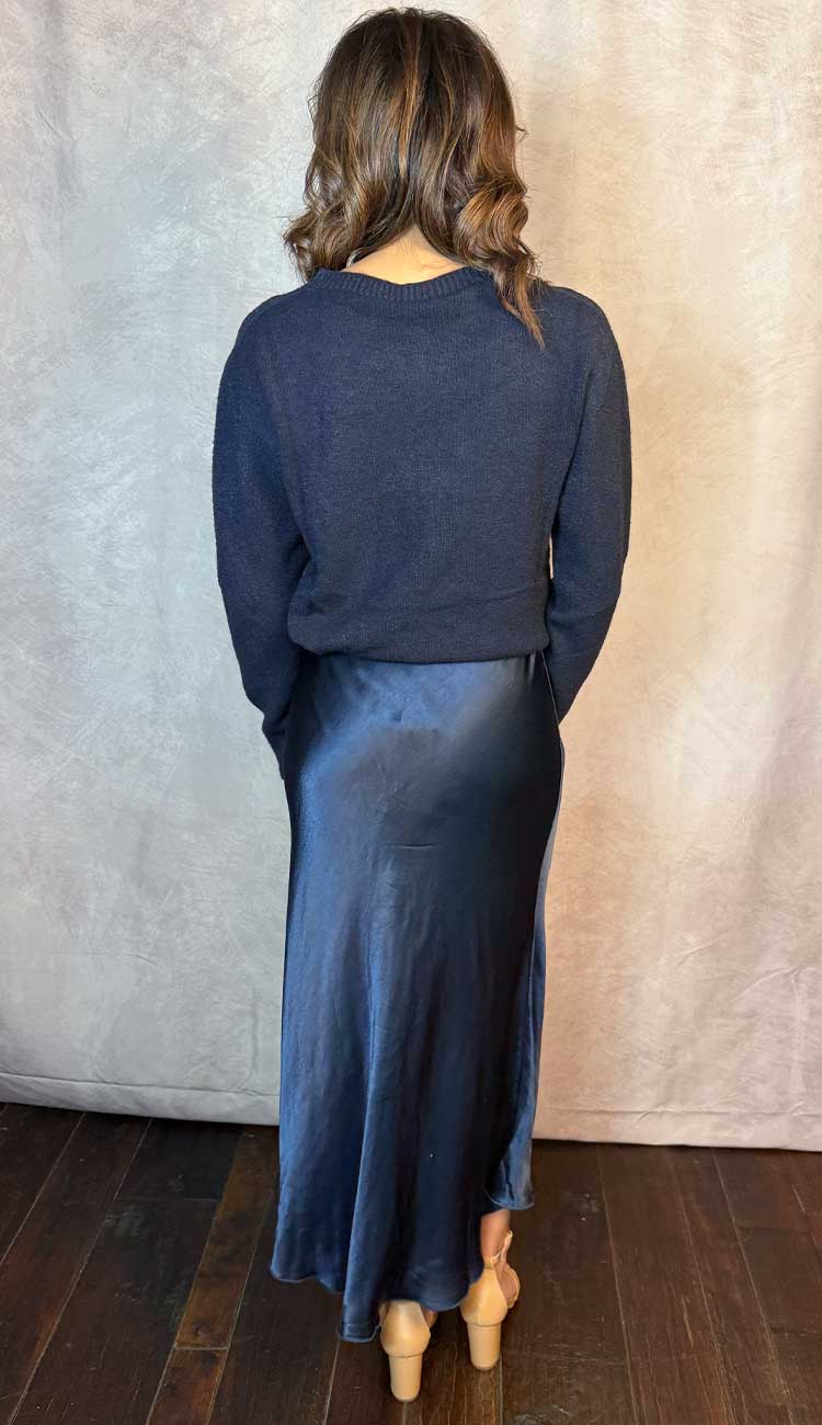 Person wearing a blue  sweater and skirt outfit standing against a textured wall.