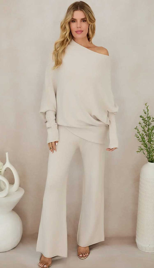 Woman wearing a beige off-shoulder top and wide-leg pants against a plain  beige background