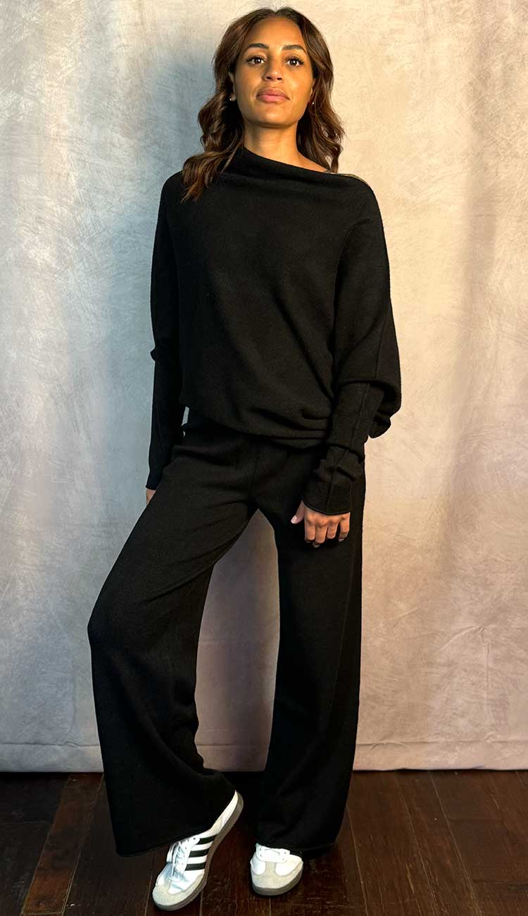 Person wearing a black outfit with white sneakers against a neutral background