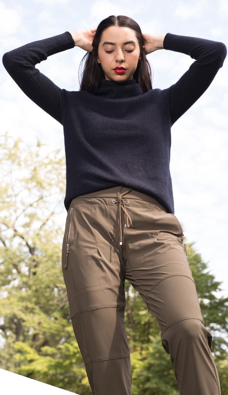 Woman wearing a black sweater and brown pants outdoors with trees in the background