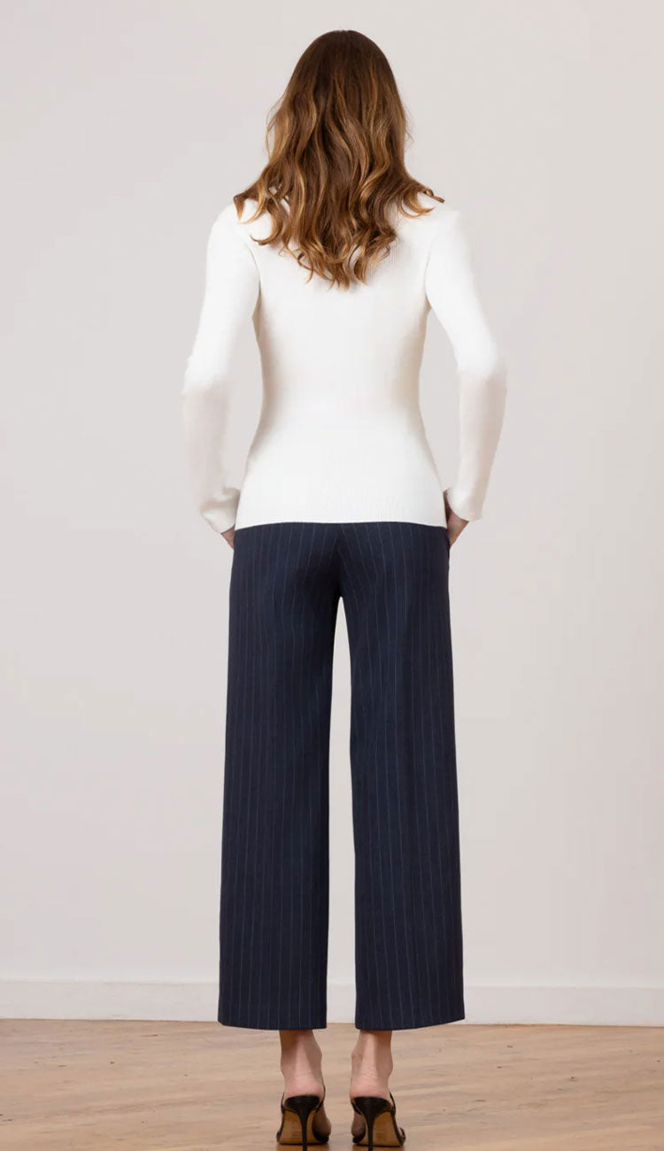 The back view of a woman wearing Grace Needle Line Navy Stripe pants with a white fitted top on a white background.
