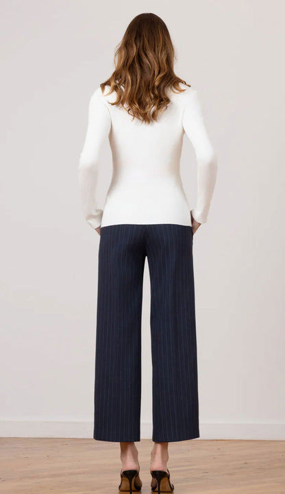 The back view of a woman wearing Grace Needle Line Navy Stripe pants with a white fitted top on a white background.