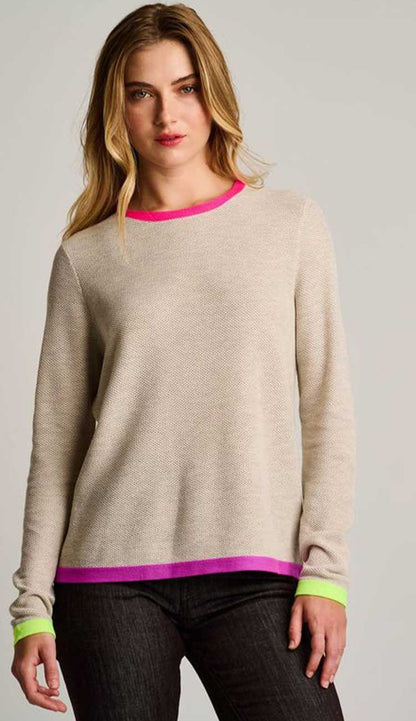 Woman wearing a beige sweater with pink and green trim on a plain background