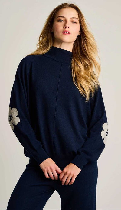 Woman wearing a navy blue sweater with floral poppy design in white on a plain background