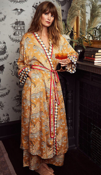 Woman wearing a Printfresh lightweight viscose robe in a tobacco leopard print, shown on a patterned background holidng a drink in her hand.