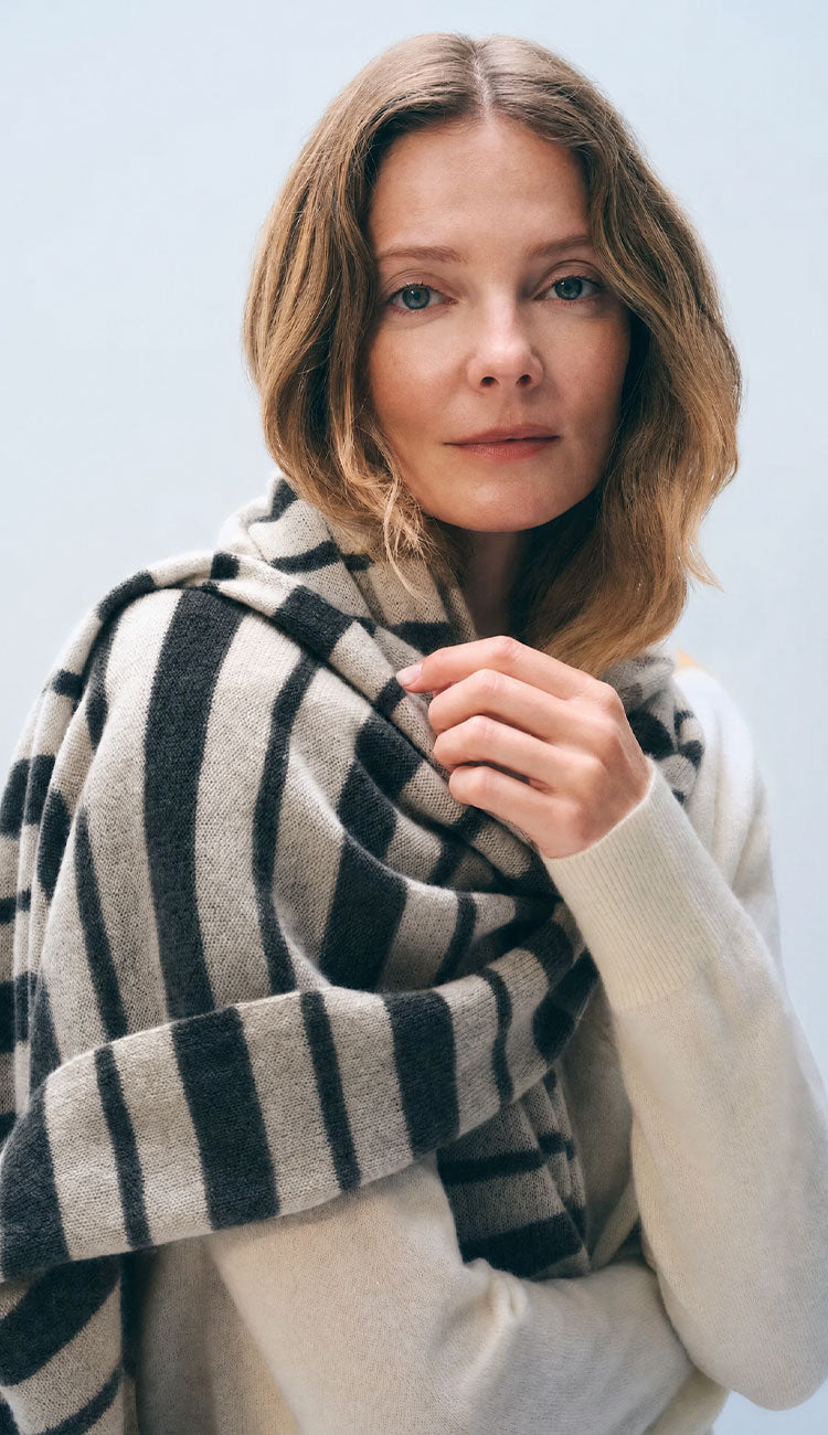 Woman wearing the White and Warren Stripe Scarf in black and taupe on a grey background.