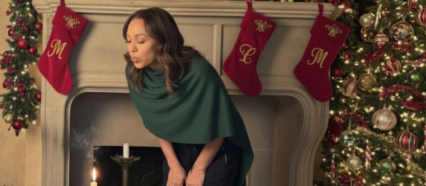 Woman in a green shawl standing in front of a decorated Christmas fireplace with stockings.