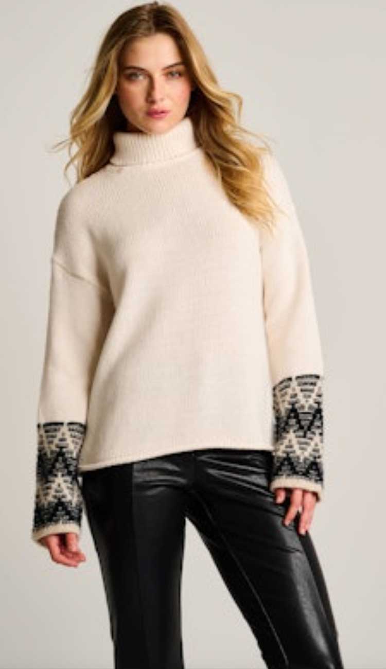 Woman wearing a cream sweater with patterned cuffs and hem on a plain background