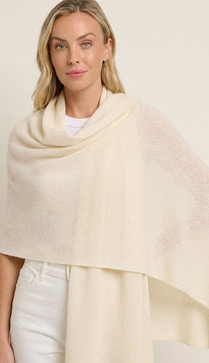 Woman wearing a cream-colored alashan breezy travel wrap over a white outfit on a plain background