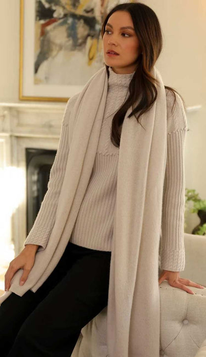 alashan cashmere breezy travel wrap | paula and chlo Champagne model wearing a matching sweater sitting on the side of a couch