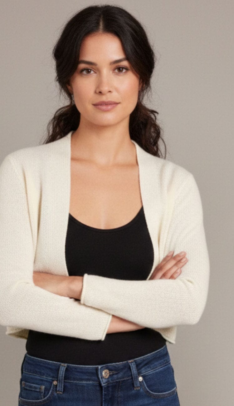 Woman standing wearing an Alashan Cashmere cropped 100% cashmere shrunken cardigan in white with long sleeves and an open-front design