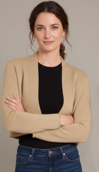 Woman standing wearing an Alashan Cashmere cropped 100% cashmere shrunken cardigan in chai with long sleeves and an open-front design.