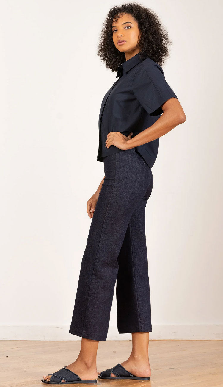 Side view of a Woman wearing a dark denim shirt and Alex dark denim pants against a textured wall. 