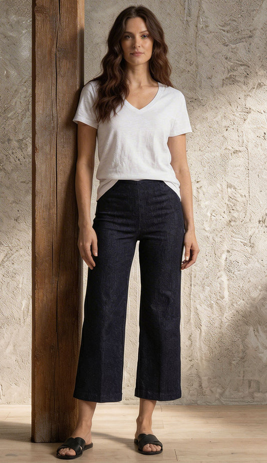 Woman wearing a white Goldie t-shirt and Alex dark denim pants against a textured wall.