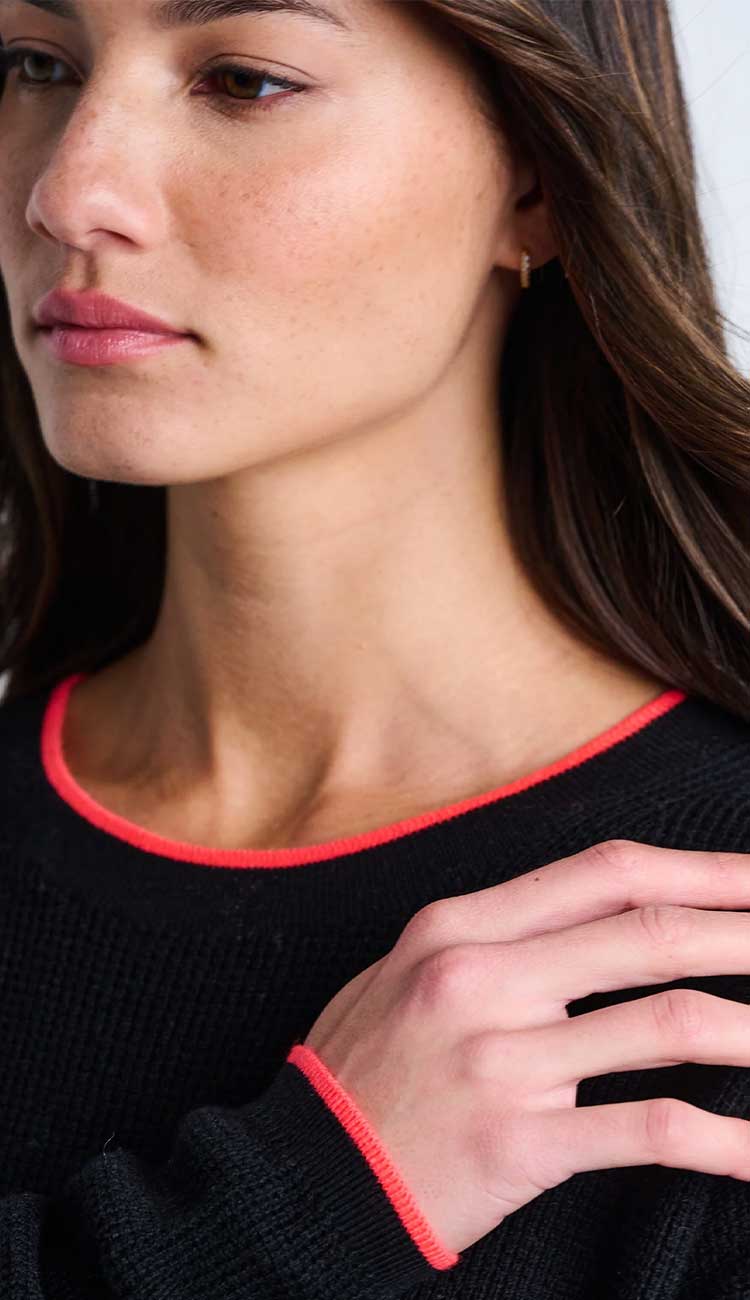 Close-up of a person wearing a black sweater with red trim.