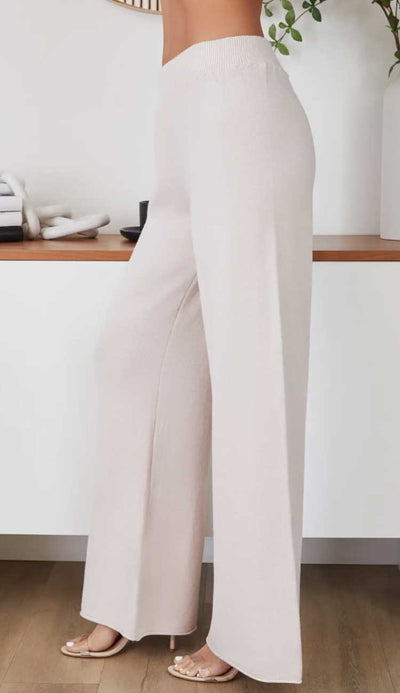 Beige wide-leg pants worn by a person in a minimal indoor setting.