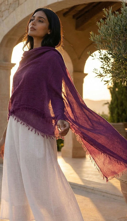 Woman wearing a purple shawl and white pants standing outdoors with a scenic background