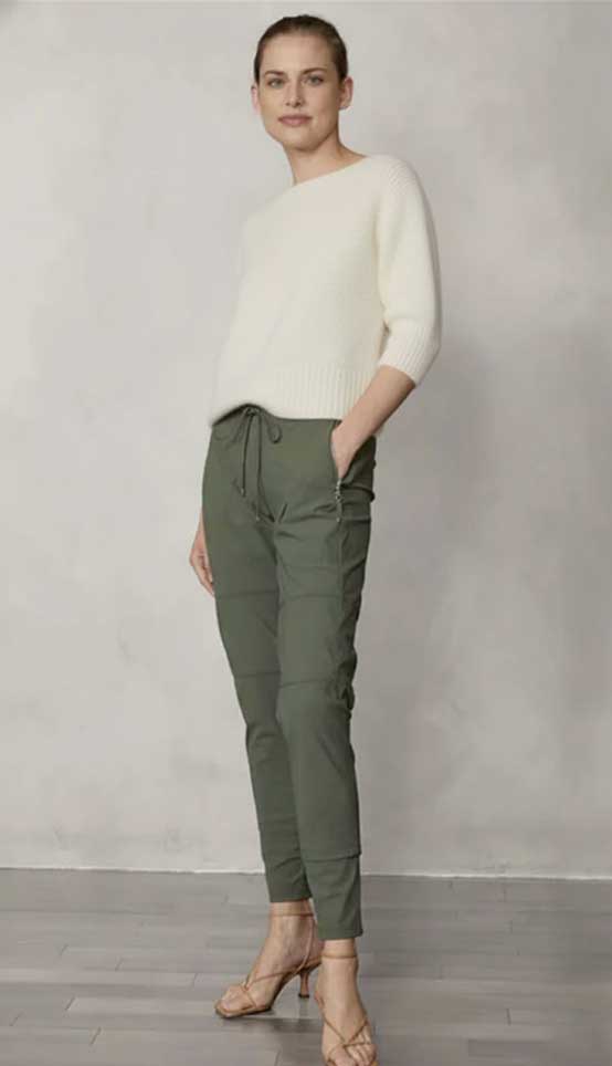 Woman wearing a white sweater and forest candy pants against a plain background