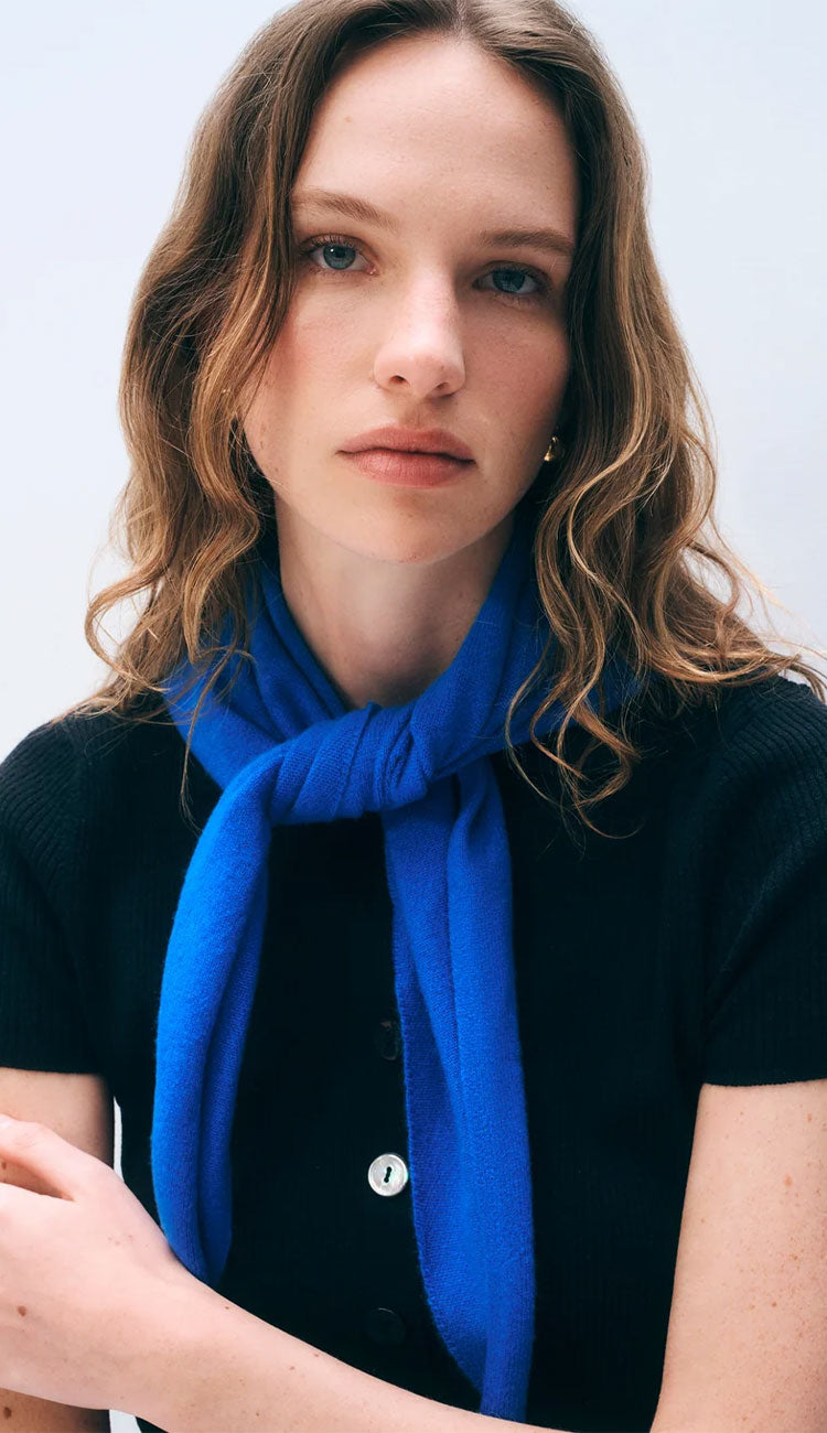 Woman wearing a white and warren cashmere neckerchief mini scarf in bright cobalt blue on a white background