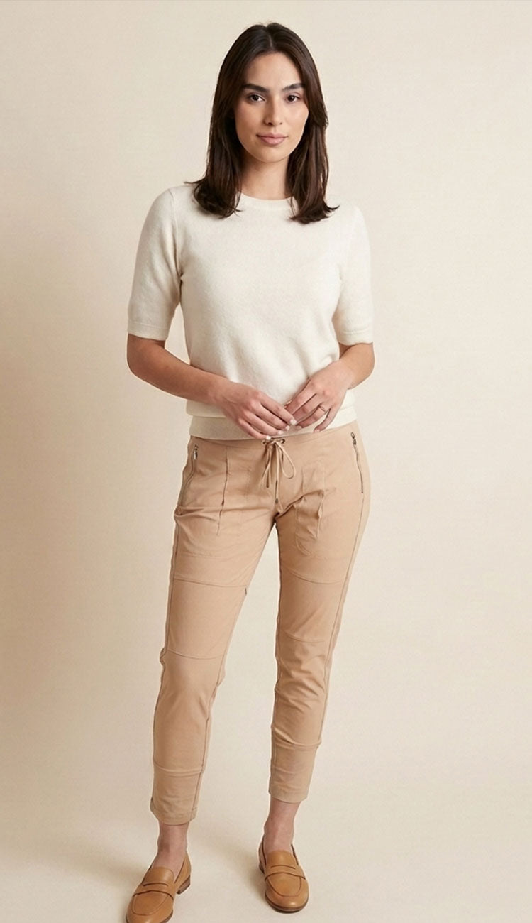 Woman wearing a white top and cashew candy pants on a plain background