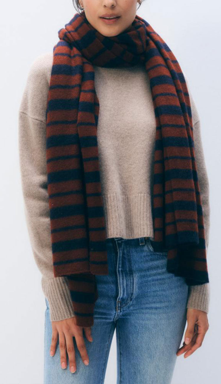 Woman wearing the White and Warren Stripe Scarf in cognac and navy on a grey background.