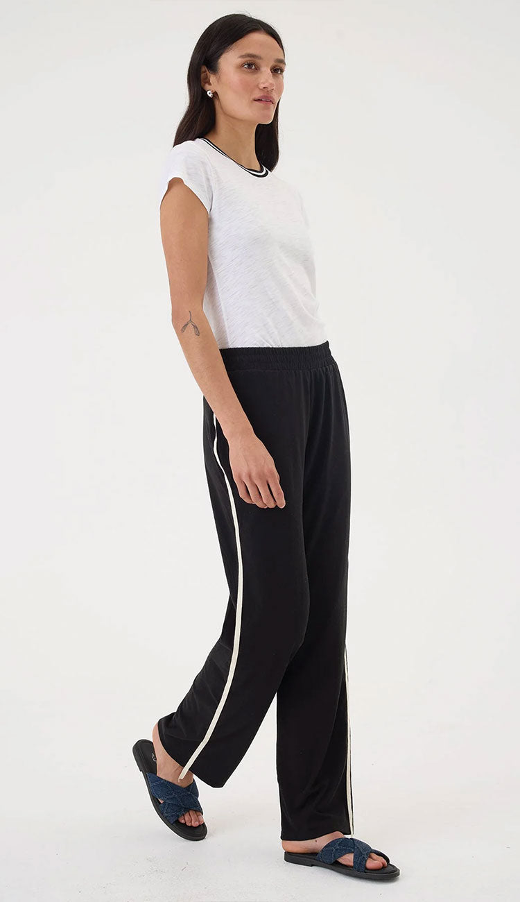 Woman wearing a white top and  Goldie Everyday black pants with a white stripe on a white background