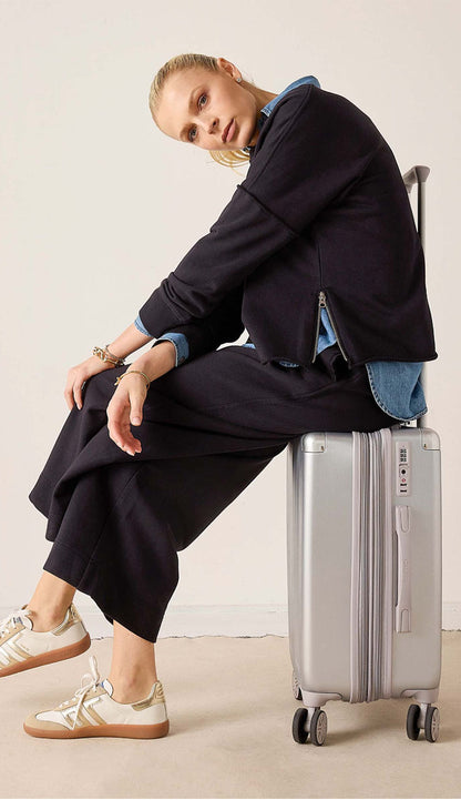 Woman wearing the frenchie zip crewneck sitting on a suitcase, wearing a pair of wide zip