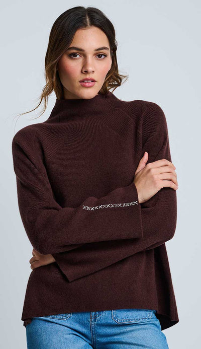 Woman wearing the Lisa Todd High Society cashmere sweater in rich  brown with a cross-stitch detail on a light gray background 