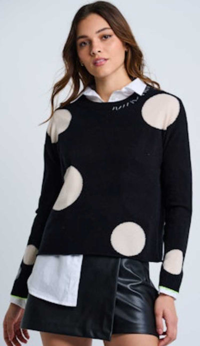Woman wearing a black sweater with winter white polka dots on a light grey background. 