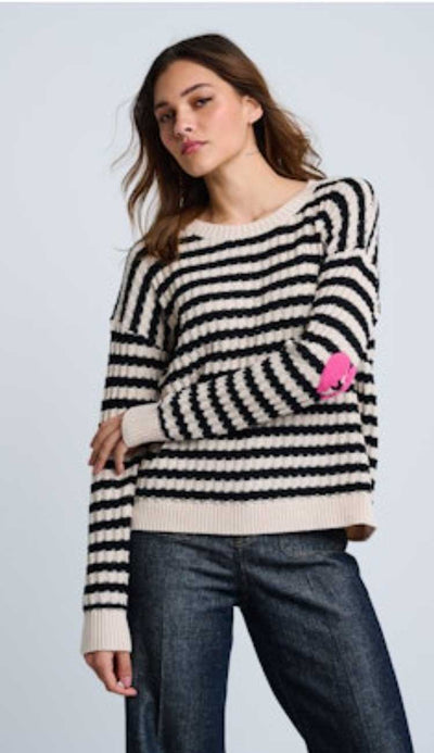 Woman wearing a black and white striped sweater with a pink broken heart on the sleeve on a light blue background