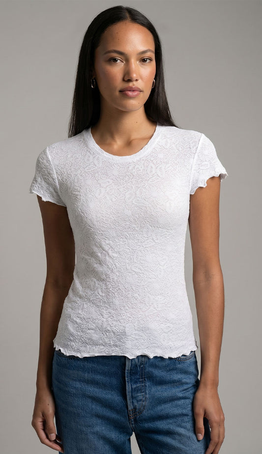 Woman wearing a white textured t-shirt  by Goldie and blue jeans against a gray background