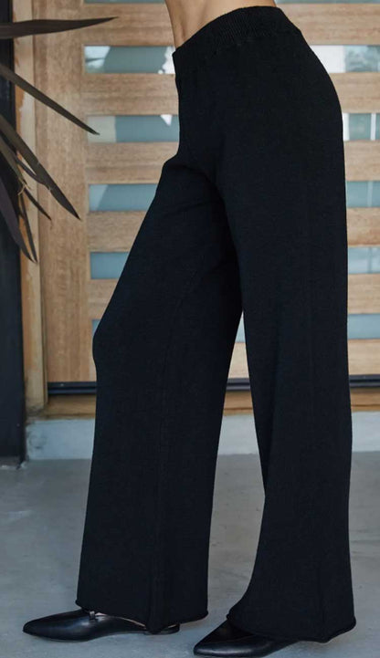 Black wide-leg pants worn by a person with a wooden panel background