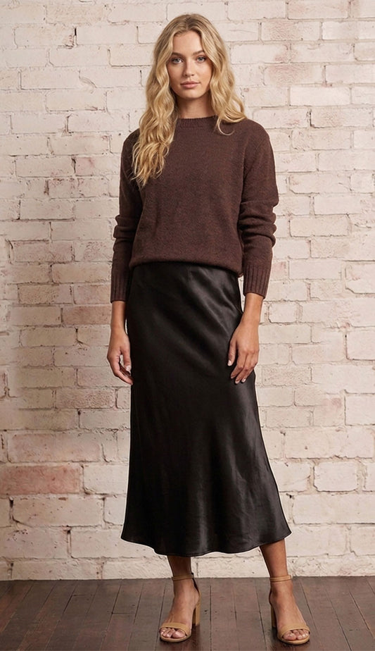 Woman wearing a brown long-sleeve top and dark brown skirt against a neutral background
