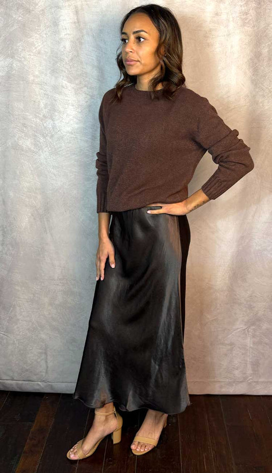 Woman wearing a brown long-sleeve sweater and brown skirt against a neutral background